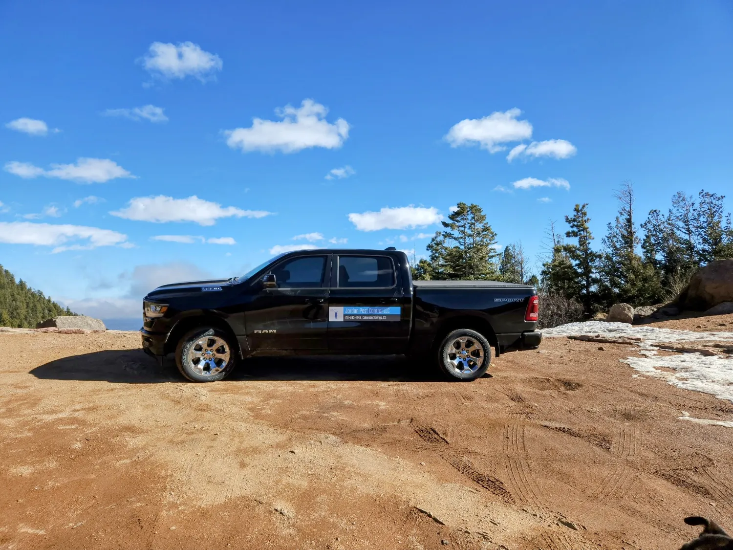 A black Ram truck parked on a dirt lot with trees in the background under a clear sky, showcasing its side profile.