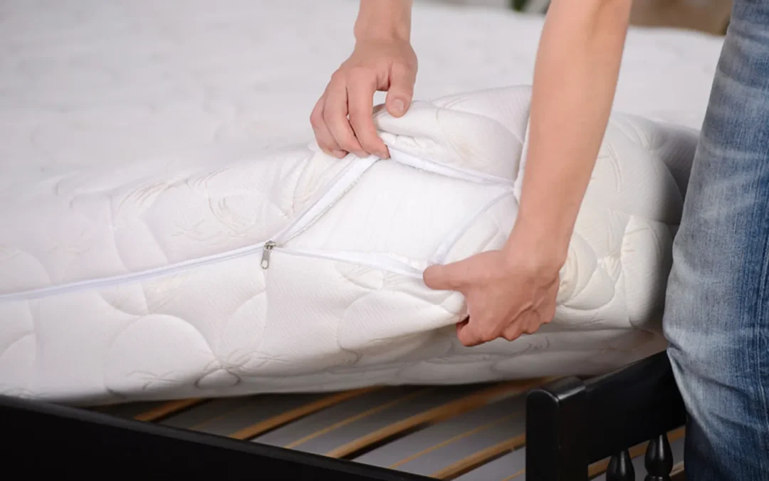 A person zips open a white mattress cover while adjusting the bedding on a black bed frame to inspect bed bugs